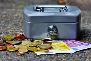 Metalowa kasetka na pieniądze z monetami i banknotami euro leżącymi obok