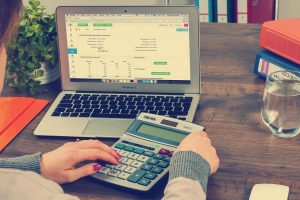 Kobieta oblicza wydatki na kalkulatorze przy laptopie z arkuszem finansowym