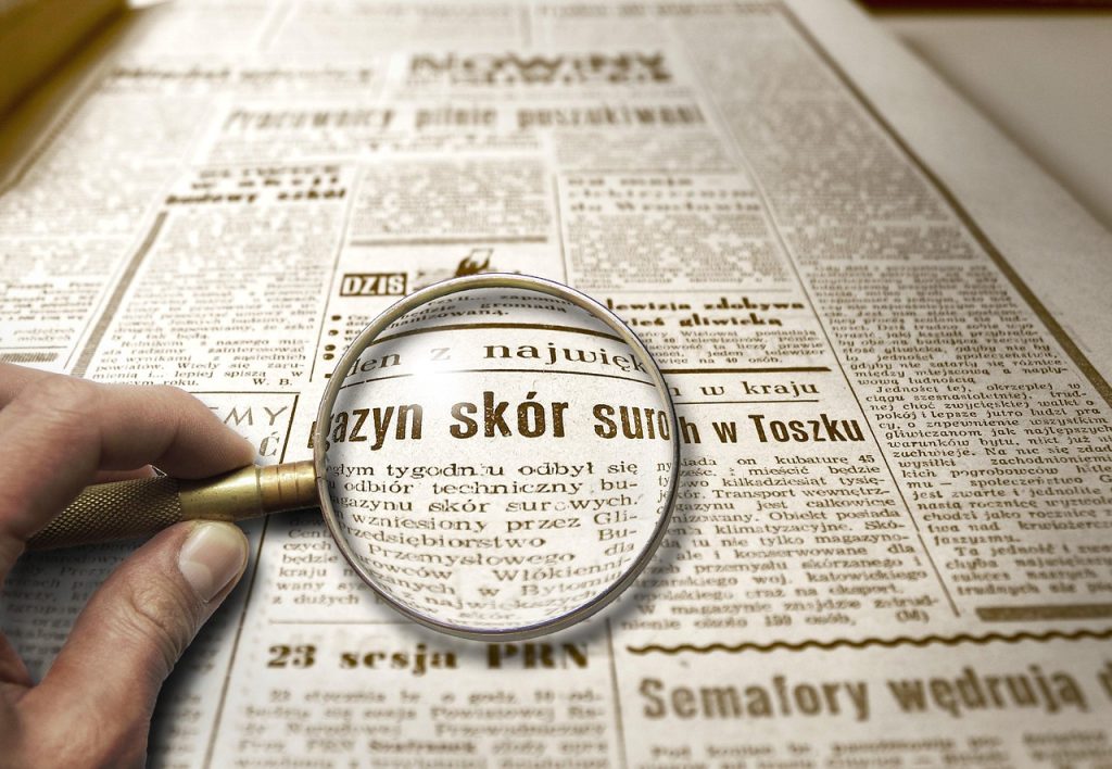 Lupa powiększająca tekst w starej gazecie, symbolizująca dokładne sprawdzanie informacji