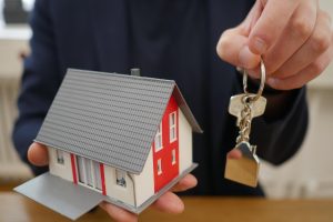 Mężczyzna trzyma model domku i klucze symbolizujące kredyt hipoteczny.